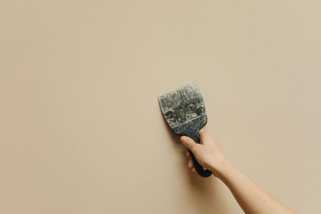 A hand holding a spatula against a blank beige wall for home renovation.